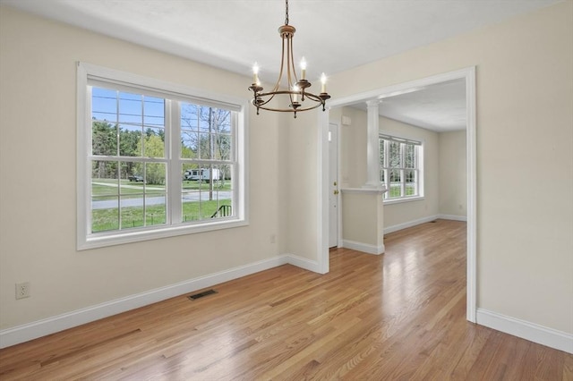 unfurnished dining area with a notable chandelier, baseboards, light wood finished floors, visible vents, and ornate columns