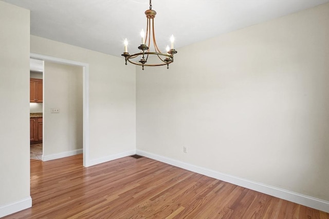 empty room with baseboards, light wood-style floors, and an inviting chandelier