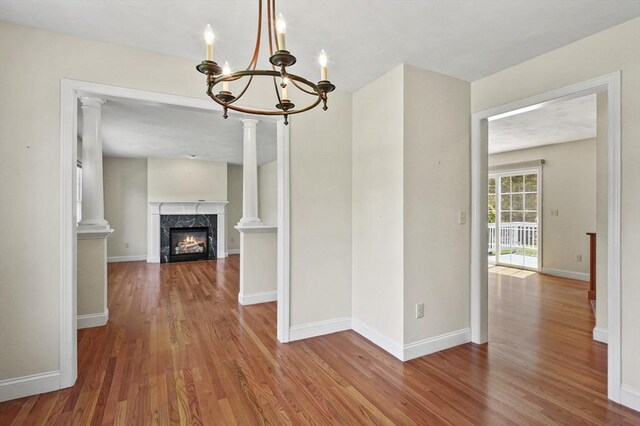 unfurnished dining area with baseboards, a fireplace, an inviting chandelier, and wood finished floors