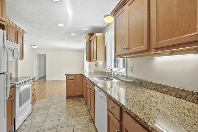 kitchen with brown cabinets, a sink, white appliances, light stone counters, and recessed lighting