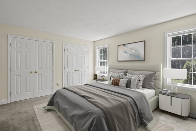 bedroom with light carpet, baseboards, and multiple closets