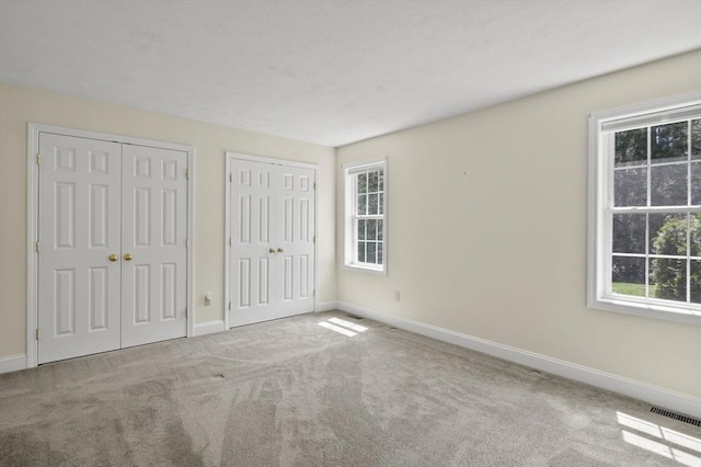 unfurnished bedroom with multiple windows, carpet, baseboards, and multiple closets