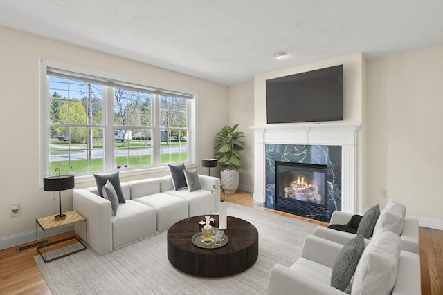 living area featuring a premium fireplace, baseboards, visible vents, and wood finished floors