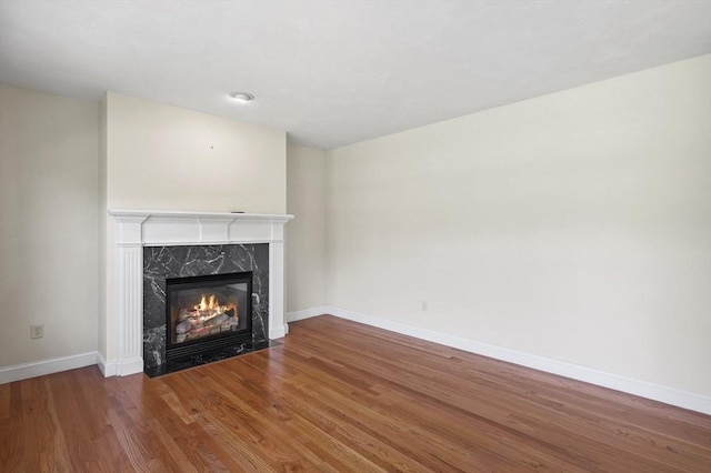 unfurnished living room featuring a premium fireplace, baseboards, and wood finished floors