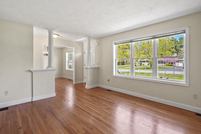 unfurnished living room featuring wood finished floors, visible vents, baseboards, and decorative columns