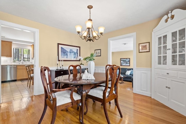 dining space with light wood finished floors, a wainscoted wall, and a notable chandelier