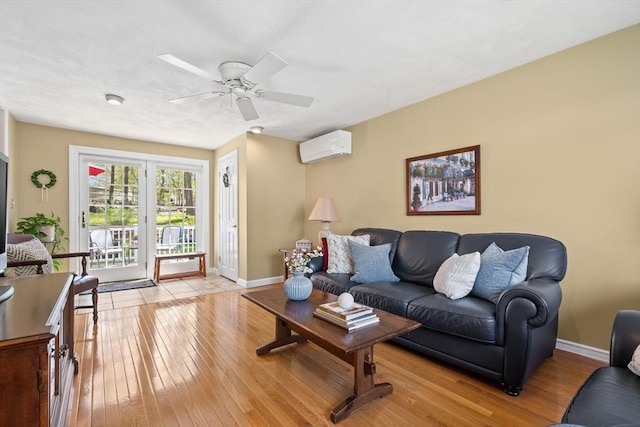 living room featuring baseboards, a wall unit AC, a ceiling fan, and light wood-style flooring