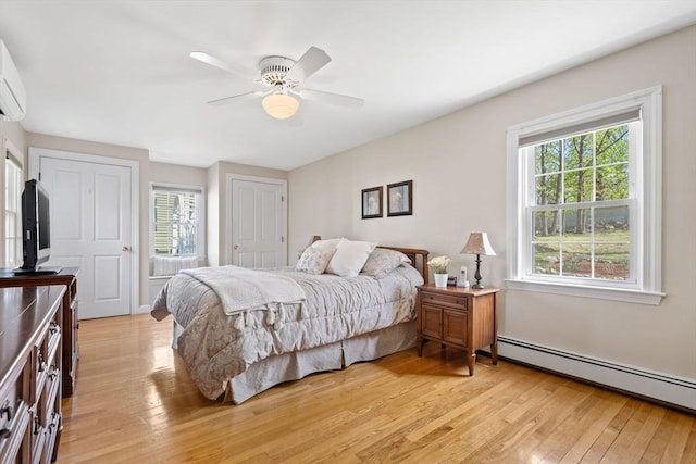 bedroom with two closets, ceiling fan, baseboard heating, and light wood-style flooring