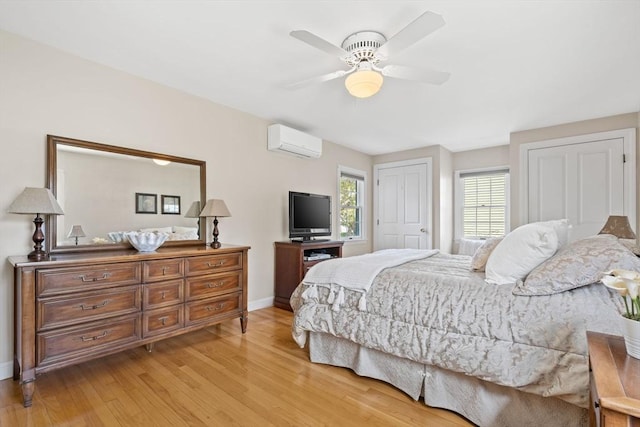 bedroom featuring a ceiling fan, baseboards, a wall unit AC, and light wood-style flooring