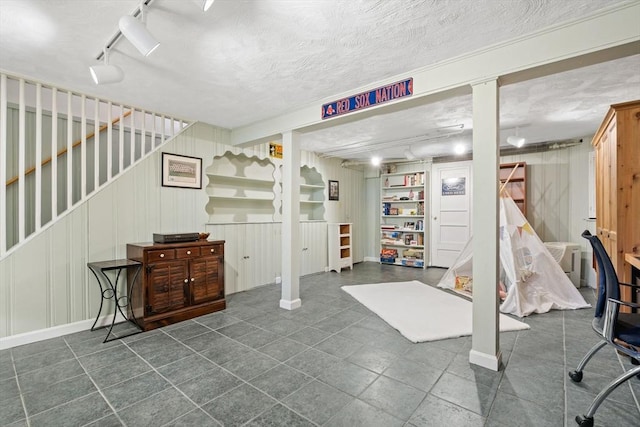 finished basement with track lighting, a textured ceiling, baseboards, and stairway
