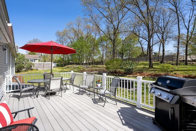 wooden deck featuring a lawn, fence, outdoor dining area, and a grill