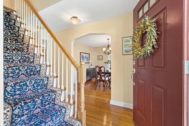 foyer entrance with an inviting chandelier, light wood finished floors, arched walkways, stairs, and baseboards