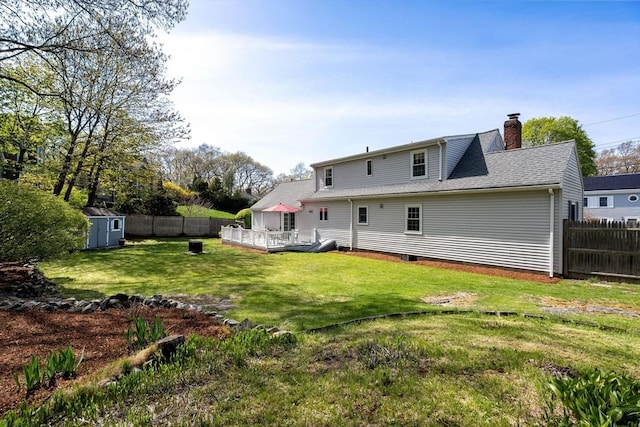 rear view of house with an outdoor structure, a wooden deck, a fenced backyard, a chimney, and a storage unit