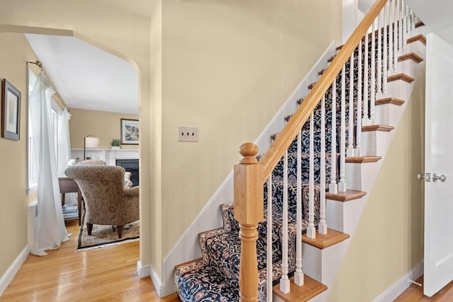 staircase with a glass covered fireplace, baseboards, and wood finished floors