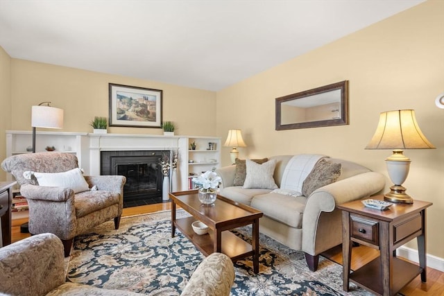 living room featuring a fireplace with flush hearth, baseboards, and wood finished floors