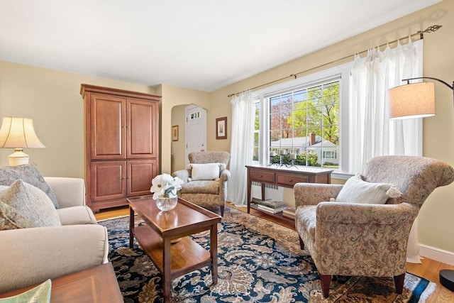 living room featuring arched walkways, baseboards, and wood finished floors
