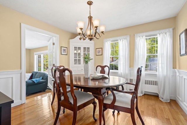 dining room with plenty of natural light, light wood-style flooring, a wainscoted wall, and a notable chandelier
