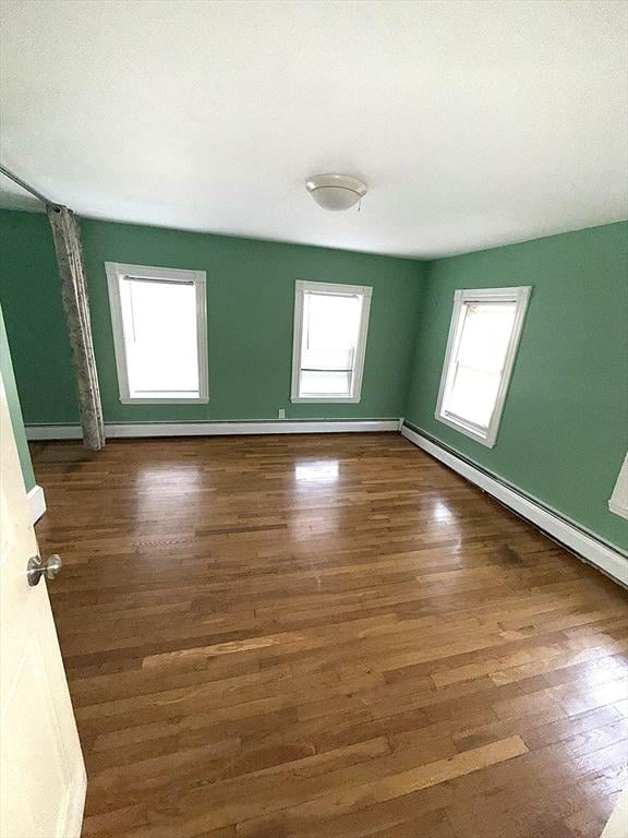 empty room with dark hardwood / wood-style floors and a baseboard heating unit