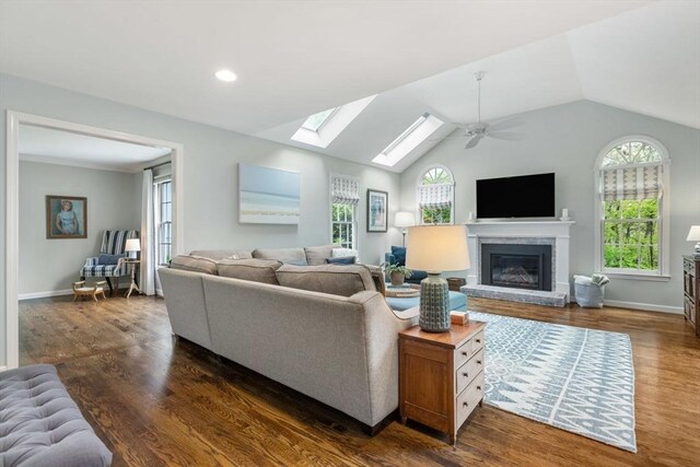 living room with dark wood-style flooring, vaulted ceiling, a glass covered fireplace, a skylight, and ceiling fan