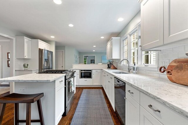 kitchen with stainless steel appliances, a sink, white cabinetry, light stone counters, and recessed lighting