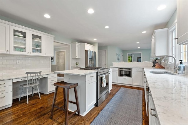 kitchen with appliances with stainless steel finishes, a sink, white cabinetry, backsplash, and light stone countertops