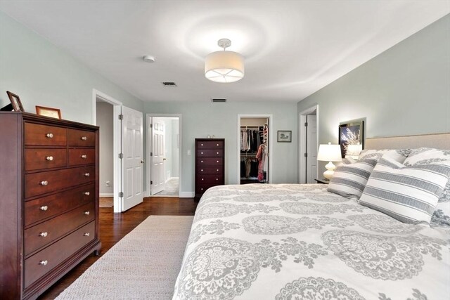 bedroom with a walk in closet, dark wood-style floors, a closet, and baseboards