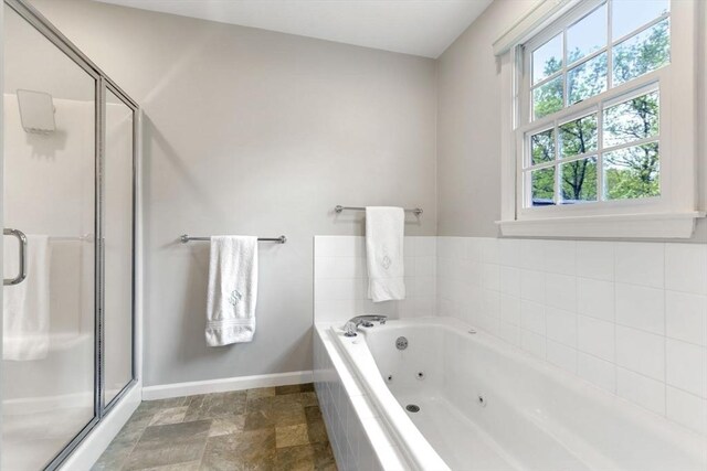 bathroom with baseboards, a stall shower, a jetted tub, and stone finish flooring