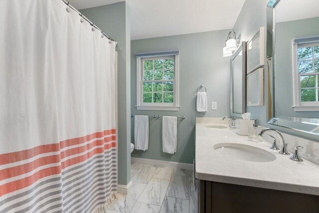 full bath featuring marble look tile flooring, toilet, double vanity, and baseboards