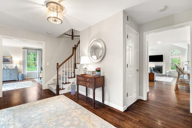 entryway with wood finished floors, baseboards, stairs, and a fireplace