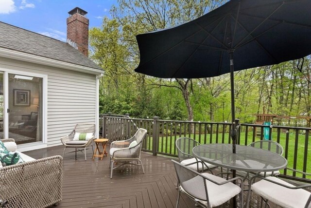 wooden terrace with outdoor dining area and a lawn