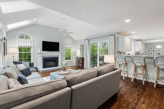 living room featuring healthy amount of natural light, a ceiling fan, dark wood finished floors, a glass covered fireplace, and vaulted ceiling