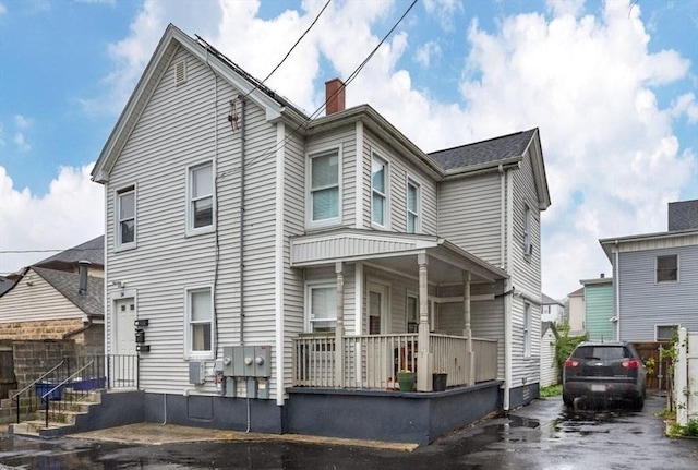 view of front of property featuring covered porch, a chimney, and fence