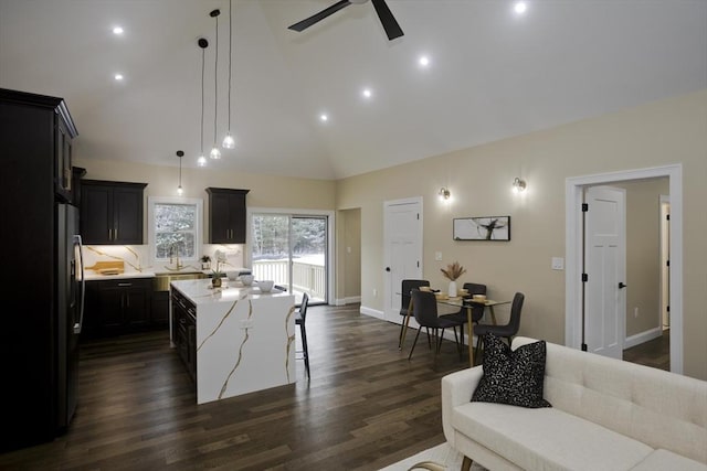 kitchen featuring hanging light fixtures, dark hardwood / wood-style flooring, light stone countertops, a kitchen island with sink, and high vaulted ceiling