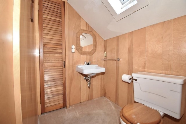 bathroom featuring toilet, sink, vaulted ceiling, and wood walls