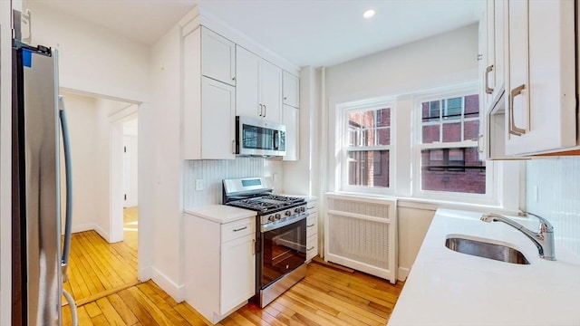 kitchen featuring decorative backsplash, a sink, appliances with stainless steel finishes, and light wood-type flooring