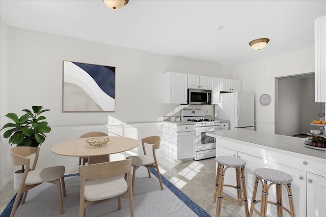 kitchen with white appliances, white cabinetry, light tile patterned flooring, and a breakfast bar area