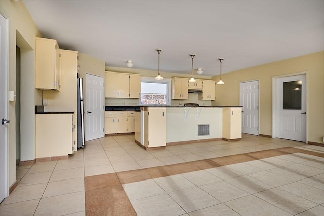 kitchen with dark countertops, visible vents, light tile patterned floors, cream cabinets, and freestanding refrigerator