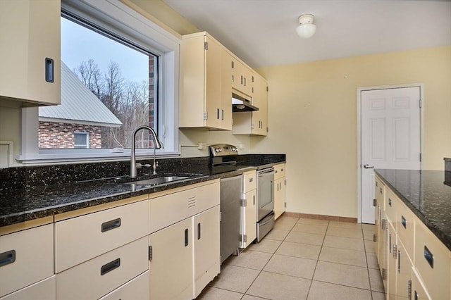 kitchen with dark stone countertops, light tile patterned flooring, a sink, stainless steel appliances, and under cabinet range hood