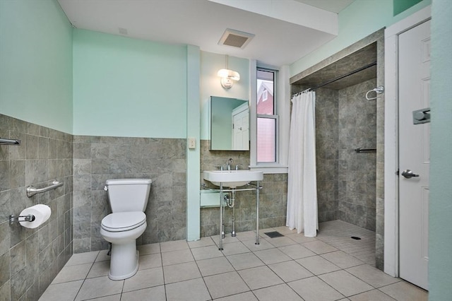 bathroom featuring a tile shower, toilet, tile walls, and a sink