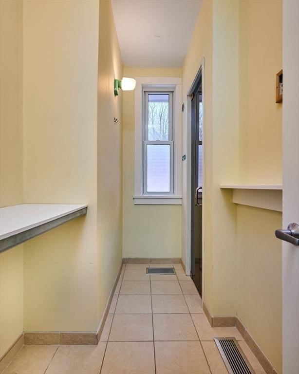 corridor featuring light tile patterned floors, visible vents, and baseboards