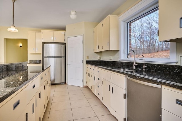 kitchen with a sink, appliances with stainless steel finishes, light tile patterned flooring, and dark stone countertops