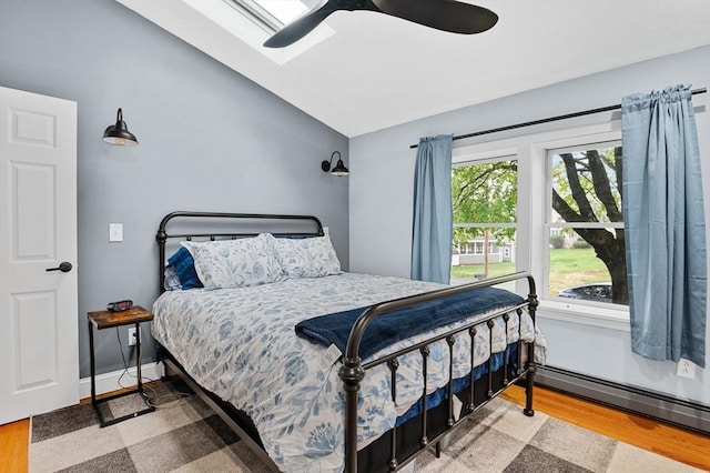 bedroom featuring wood finished floors, vaulted ceiling, a baseboard radiator, and ceiling fan