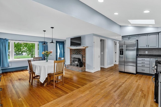 dining room with a wood stove, a skylight, a baseboard radiator, light wood-style flooring, and baseboards