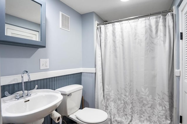 bathroom featuring a sink, a wainscoted wall, toilet, and a shower with curtain
