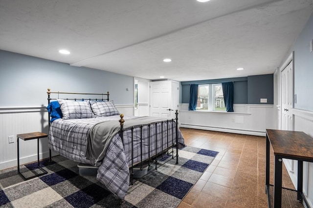 tiled bedroom with a baseboard radiator, a wainscoted wall, recessed lighting, and a decorative wall