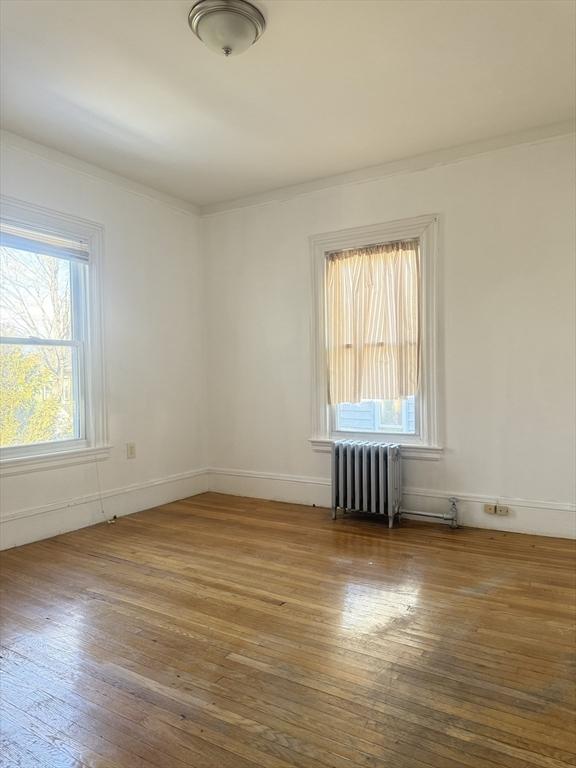 unfurnished room with hardwood / wood-style flooring, crown molding, and radiator