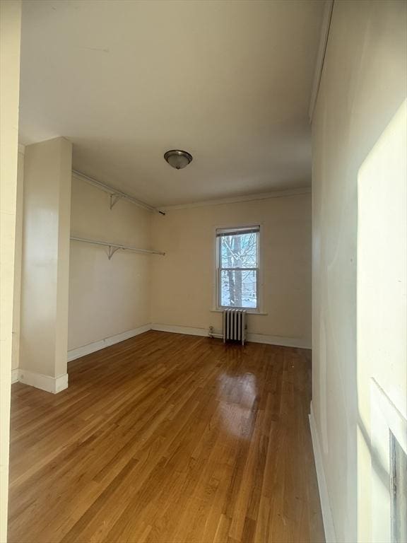 empty room featuring hardwood / wood-style flooring, crown molding, and radiator heating unit