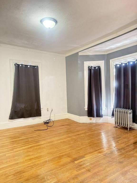 empty room featuring crown molding, radiator, and light wood-type flooring