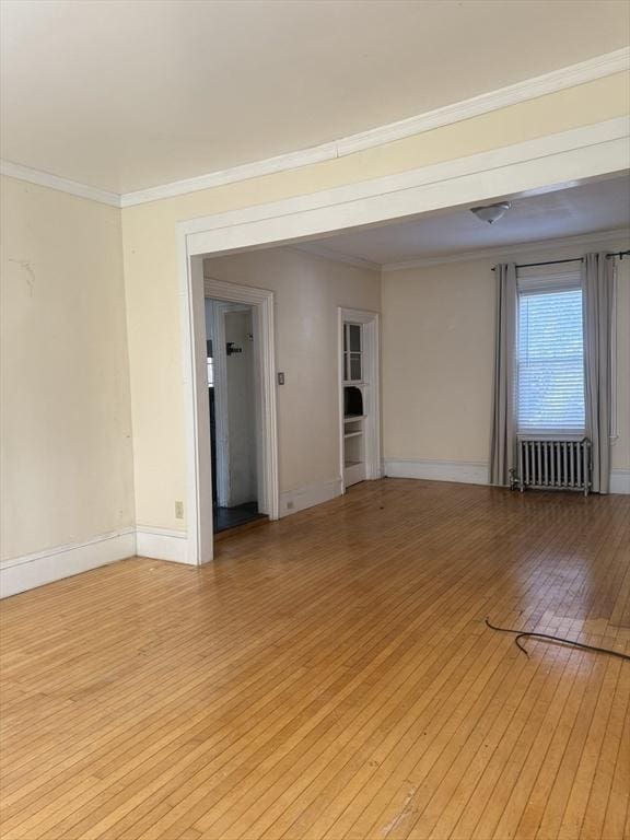 empty room featuring ornamental molding, radiator, and light wood-type flooring