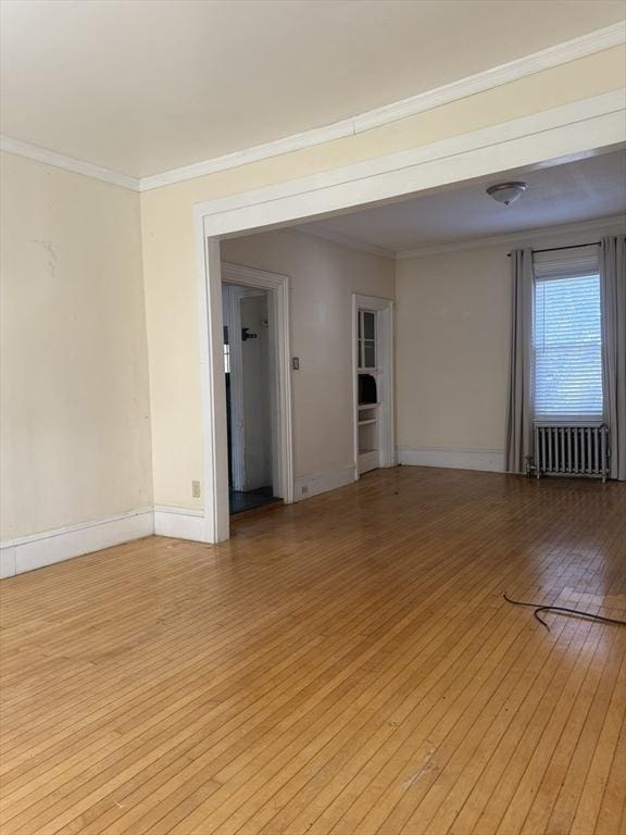 empty room featuring crown molding, radiator heating unit, and light hardwood / wood-style floors